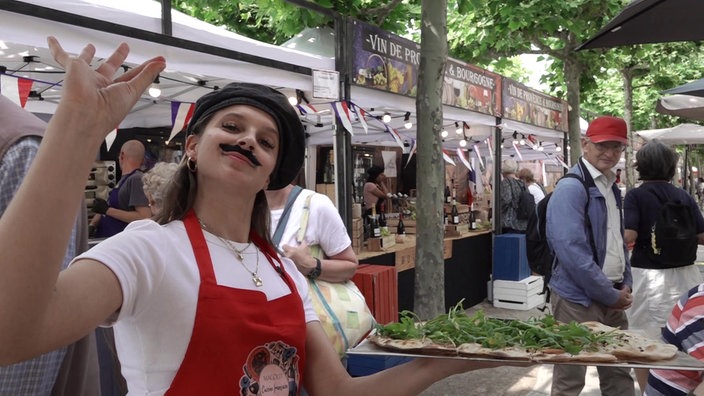 Eine Händlerin in einem französischen Outfit serviert Flammkuchen.
