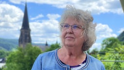 Eine Frau schaut in die Ferne, im Hintergrund ist blauer Himmel und ein Kirchturm.