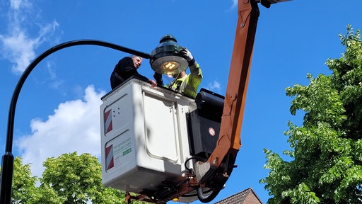 Zwei Männer in einem Hubwagen in der Luft an einer Gasleuchte