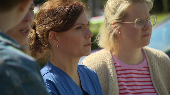 Mehrere Frauen stehen auf einem Parkplatz und blicken ernst in Richtung der Klinik in Kempen