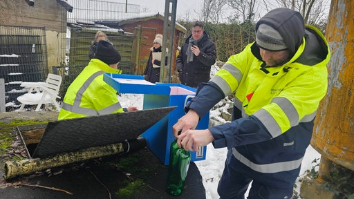 Ein Mitarbeiter der Bergbehörde der Bezirksregierung Arnsberg nimmt Wasserproben auf dem Kleingartengelände. Einer von ihnen stellt zwei Flaschen auf einem Tisch vor einer blauen Box ab.
