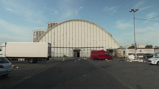 Vorderseite einer weißen Halle und Fahrzeuge auf Parkplatz