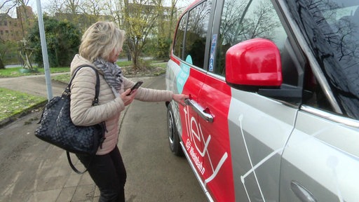 Ein Frau mit Handy in der Hand will die Tür eines Kleinbusses öffnen