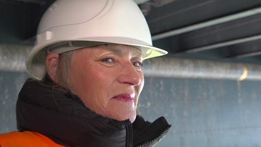 Eine Frau unter einer Brücke in dicker Jacke und mit weißem Bauhelm