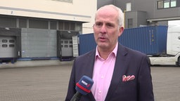 Ein Mann im Anzug und pinkem Hemd auf einem großen Betriebshof