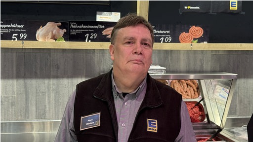 Mann in Edeka-Weste hinter Fleischtheke 