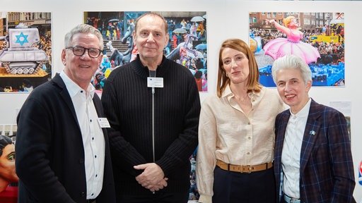Vier Menschen posieren vor aufgestellten Wänden mit Fotos