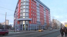 Ein großes Gebäude, davor eine befahrene Straße und Fußgänger