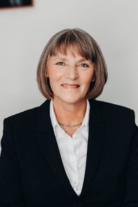 Eine Frau mit mittellangen, gräulichen Haaren, weißer Bluse und dunklem Blazer