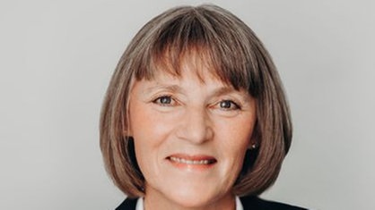 Eine Frau mit mittellangen, gräulichen Haaren, weißer Bluse und dunklem Blazer