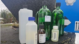 Mehrere Plastik- und Glasflaschen stehen nebeneinander. Einige sind mit einem Etikett mit der Aufschrift "PAK" beklebt.