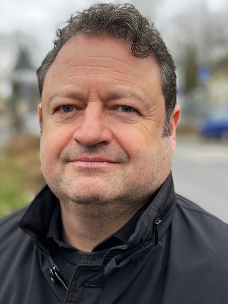 Jens Franke, ein grauhaariger Mann mit Dreitagebart steht draußen auf einem Gehweg und lächelt freundlich.