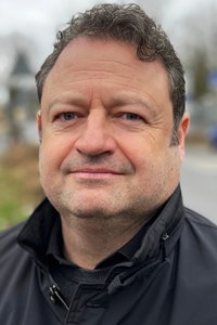 Jens Franke, ein grauhaariger Mann mit Dreitagebart steht draußen auf einem Gehweg und lächelt freundlich.