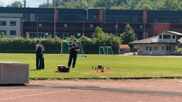 Zu sehen sind drei Feuerwehrleute und eine Drohne auf einem Sportplatz.