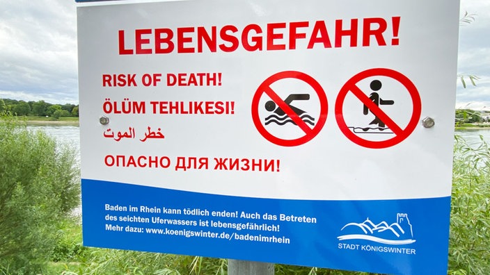 Ein Schild weist mit großen, roten Buchstaben auf verschiedenen Sprachen auf die Lebensgefahr beim Schwimmen im Rhein hin.
