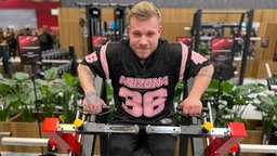 Ein Mann sitzt an einem Fitnessgerät zum Muskelaufbau
