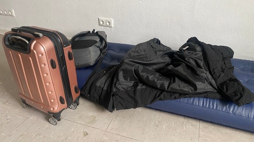 Ein kleiner Rollkoffer, ein Rucksack und eine Jacke liegen auf einer aufgeblasenen Luftmatratze