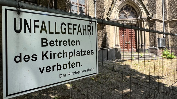 Ein Hinweisschild mit schwarzen Buchstaben, warnt vor einer Unfallgefahr am Kirchplatz. 