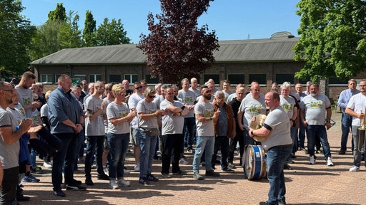 Die Mitarbeitenden des Unternehmens stehen in grauen T-Shirts versammelt auf einem Platz und klatschen.