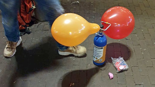 Ein Mann steht vor Ballons, die mit Lachgas gefüllt werden