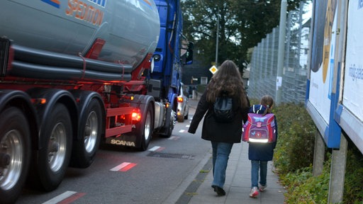 Mutter und Kind auf einem schmalen Bürgersteig neben einem Lastwagen