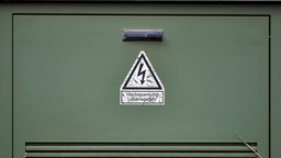 grüner Stromkasten mit Warnhinweis