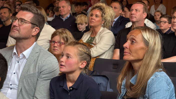 Mia sitzt zwischen ihren Eltern im Publikum und sieht auf die Bühne
