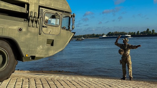 Ein Militärfahrzeug am Rheinufer, daneben ein Soldat in Uniform
