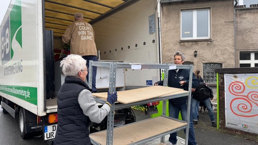Zwei Frauen beladen einen LKW mit einem Regal