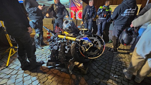 Polizisten und andere Personen stehen um ein demoliertes Motorrad