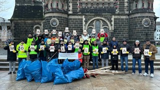 Zu sehen ist die Ahmadiyya Jugend Mönchengladbach mit einem Banner "Liebe für Alle, Hass für Keinen". Davor sind Müllsäcke mit Raketenresten der Silvesternacht.
