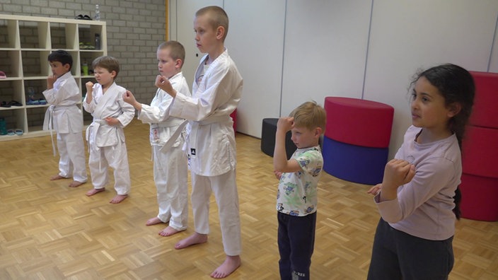 Kinder trainieren in einem Düsseldorfer Verein: Sie stehen in einem Trainingsraum in ihren Karate-Anzügen.