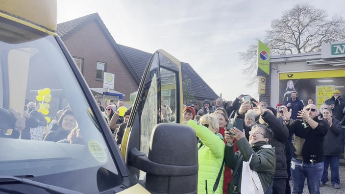 Eine Menschenmenge steht vor einem offenen Lieferwagen, applaudiert und macht Fotos.