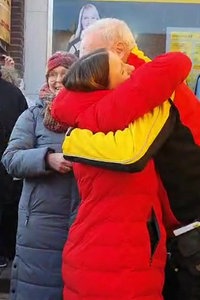 Eine Frau umarmt einen Paketboten vor seinem Lieferwagen. Drumherum stehen Menschen. 