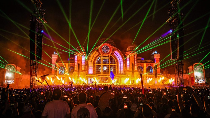 Ein großes Publikum steht vor der Parookaville-Bühne und feiern. Es ist bereits Nacht und Laser-und Feuerstrahler erhellen die Bühne.