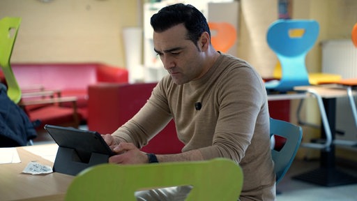 Ein Mann sitzt in einem Klassenzimmer an einem Tablet