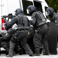 Mehrere Polizisten in Uniform und Schutzhelm verstecken sich hinter einem weißen Transporter. (Symbolfoto)