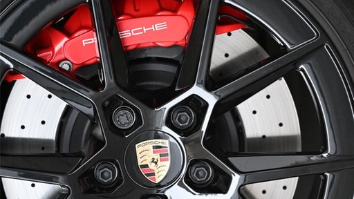 Die schwarz lackierten Streben einer Felge des Autoherstellers Porsche lassen den Blick auf die silberne Bremsscheibe und den roten Bremssattel des Rades zu