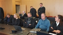 Die Angeklagten sitzen neben ihren Anwälten im Gerichtsaal. 
