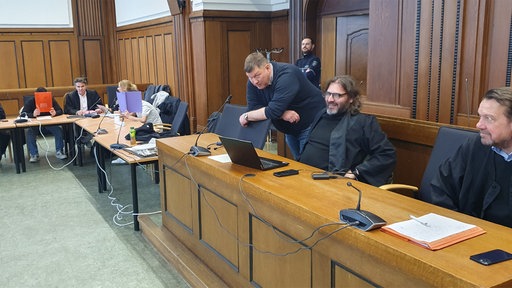 Teil der Angeklagten und ihre Verteidiger sitzen im Gerichtsaal