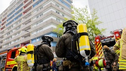 Polizeibeamte mit Gasmasken und Feuerwehrleute stehen vor einem Hochhaus in Ratingen.
