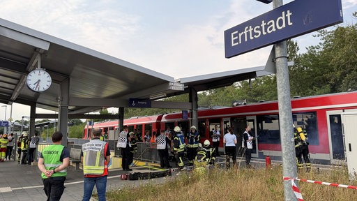 Einsatzkräfte der Feuerwehr stehen vor dem rauchenden Zug in Erftstadt.