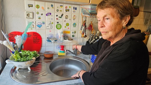 Eine Frau steht vor einem laufenden Wasserhahn.