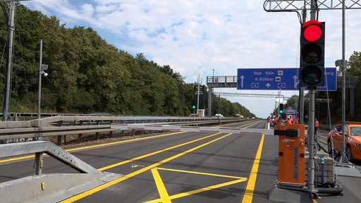 Eine rote Ampel und eine Schranke auf der Autobahn, im Hintergrund kann man ein Autobahnschild sehen