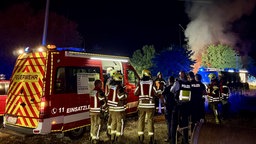 Einsatzkräfte von Polizei und Feuerwehr stehen vor Rettungsfahrzeugen. Im Hintergrund ist eine Rauchsäule.