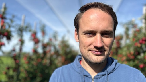 Bild eines Manns, vom Oberkörper aufwärts, mit dunklem Haar