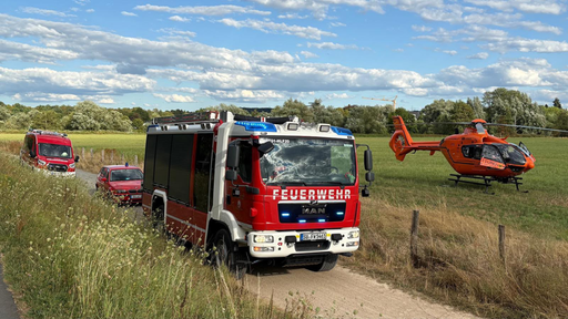 Ein rotes Feuerwehrfahrzeug, zwei weitere Einsatzwagen und ein oranger Rettungshubschrauber bei einem Einsatz.
