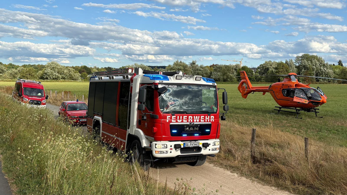 Ein rotes Feuerwehrfahrzeug, zwei weitere Einsatzwagen und ein oranger Rettungshubschrauber bei einem Einsatz.