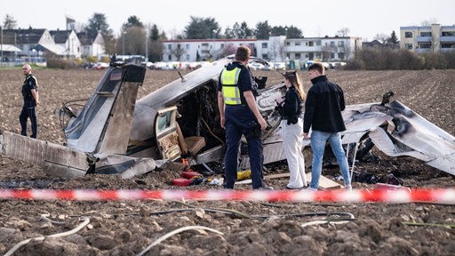 Einsatzkräfte stehen um das abgestürtze Flugzeug auf einem Acker in Sankt Augustin