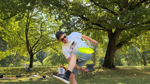Junger Mann mit weißem T-Shirt und schwarzer Kappe schwingt gelbe Frisbee-Scheibe